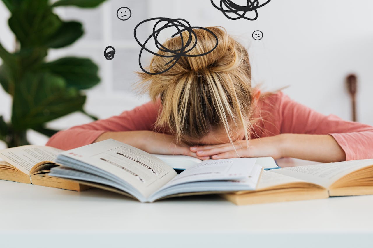 Como fugir da produtividade tóxica? 3 Mulher debruçada sobre os livros, que estão sobre uma mesa de madeira, simbolizando o cansaço causado pela produtividade tóxica.