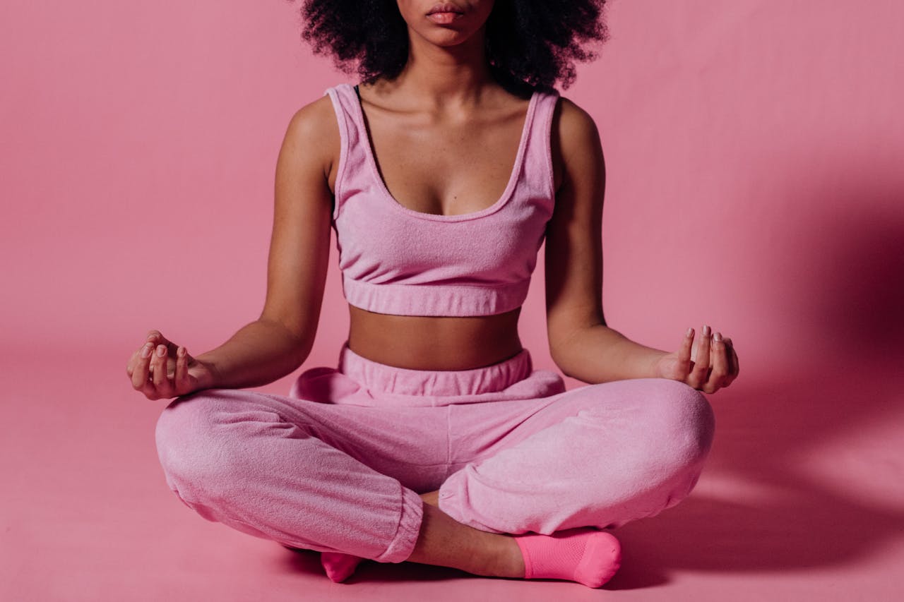 Como diminuir a ansiedade e o nervosismo: dicas práticas para o dia a dia 3 Mulher sentada no chão com uma roupa rosa e um fundo rosa praticando meditação