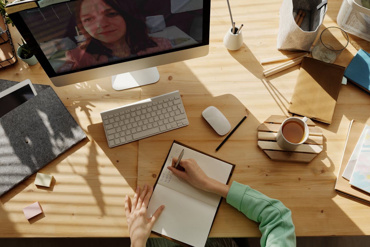 Mulher assistindo a uma aula no computador e escrevendo formulas matemáticas no caderno, representando o tópico que fala sobre o organização do ambiente de estudos